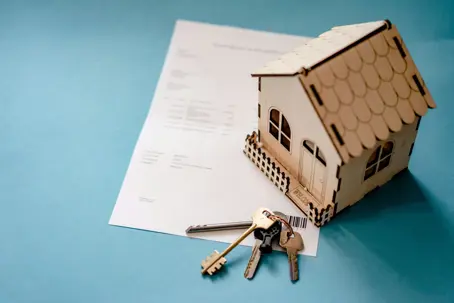 A miniature wooden home with keys next to a document